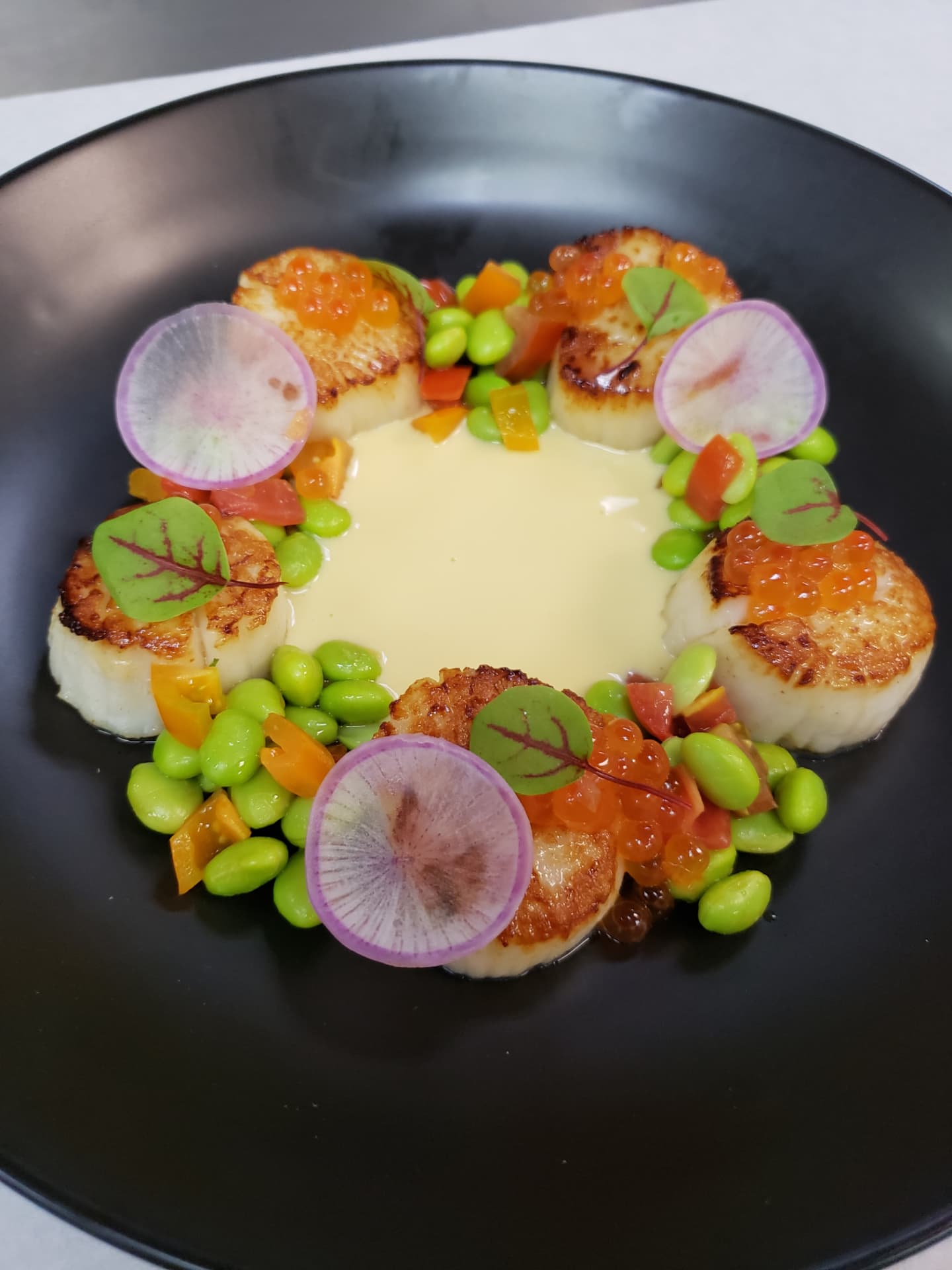 Seared scallops with edamame, radish and roe in a black bowl