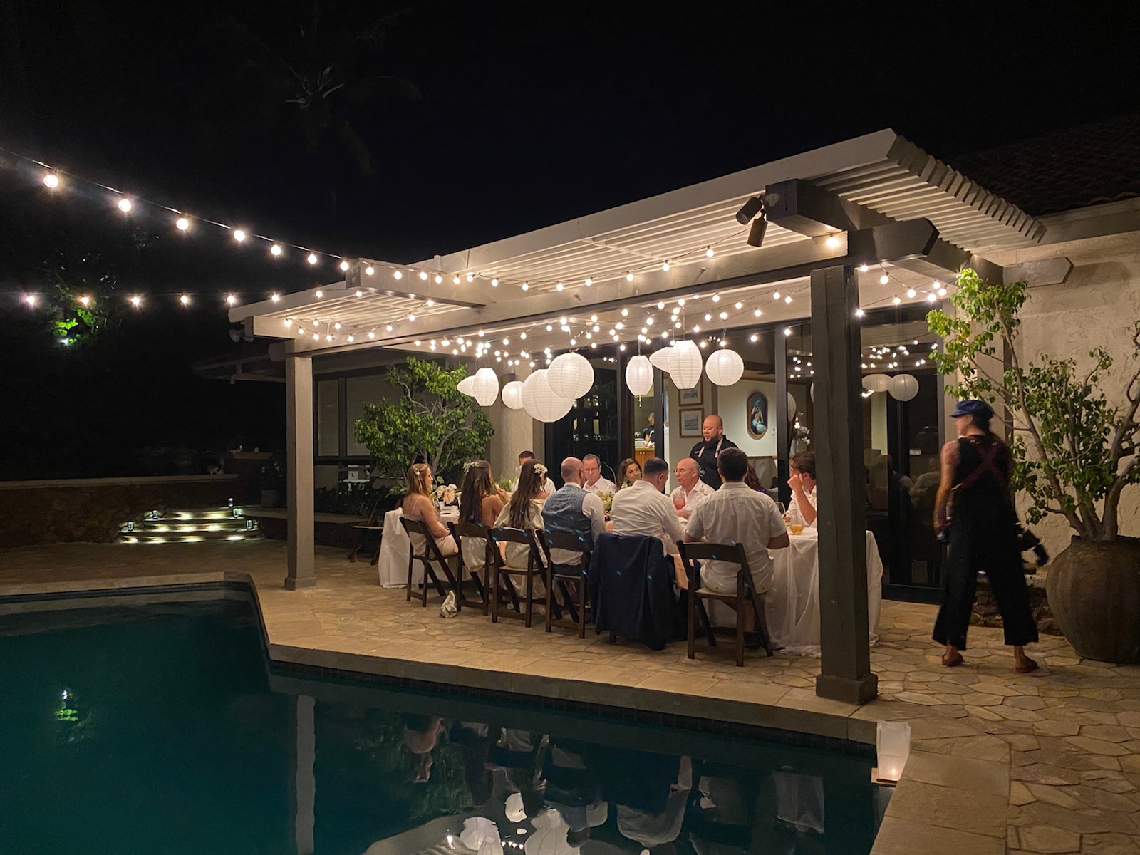 Private dinner table set beside a pool under string lights in Hawaiʻi at night