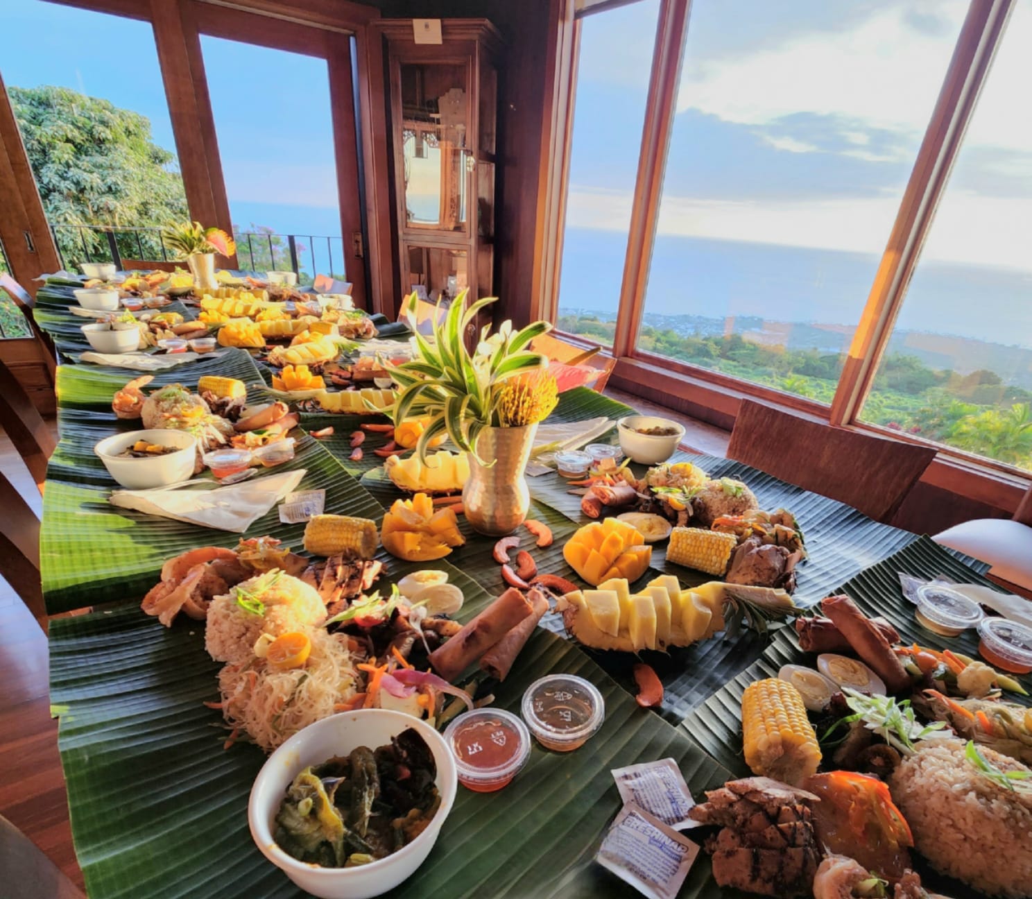 Kamayan feast laid on banana leaves along a long table facing the ocean