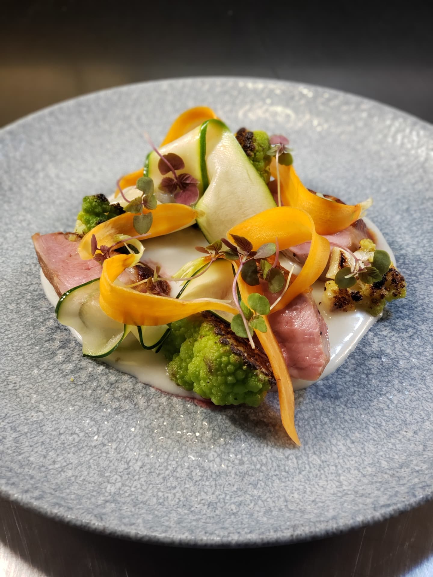 Sliced meat plated with carrot ribbons, cucumber and Romanesco